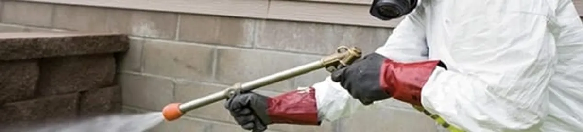 Pest control technician applying exterior insect treatment along a home foundation in Tuscaloosa, AL