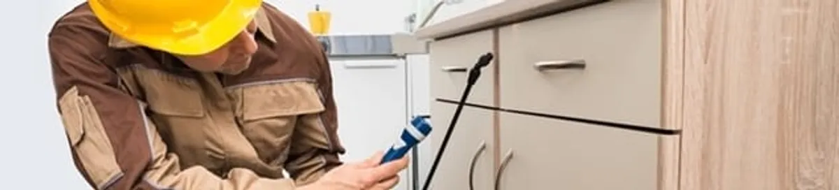 Roach exterminator applying treatment under kitchen cabinets in Tuscaloosa, AL