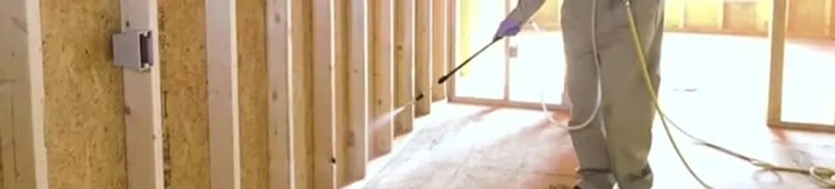 Termite treatment technician applying spray along framing and unfinished walls in Tuscaloosa, AL